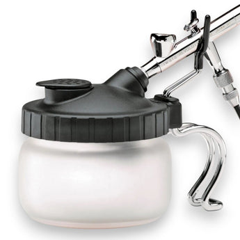 A white cleaning station can with a black ribbed screw-on lid, shown with a silver airbrush connected to the top, on a plain white background.