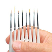 Set of small paintbrushes held between fingers against a white background